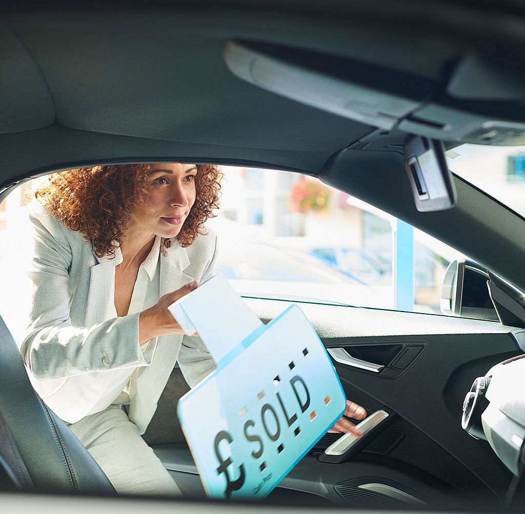 Woman adding a sold sign to a car