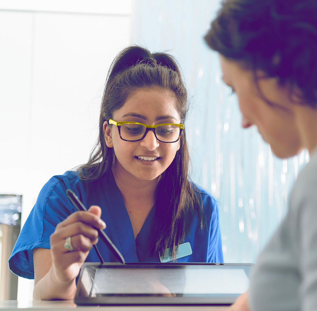 Dental receptionist assisting patient fill in form on digital tablet in dental surgery