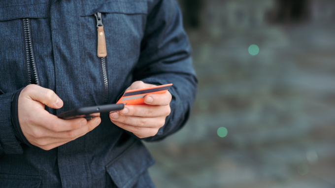 Person holding a phone and a card, appearing to make a payment